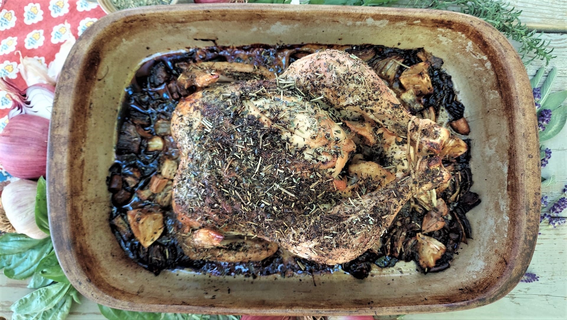 A whole roasted chicken covered with herbs in an earthware roasting pan