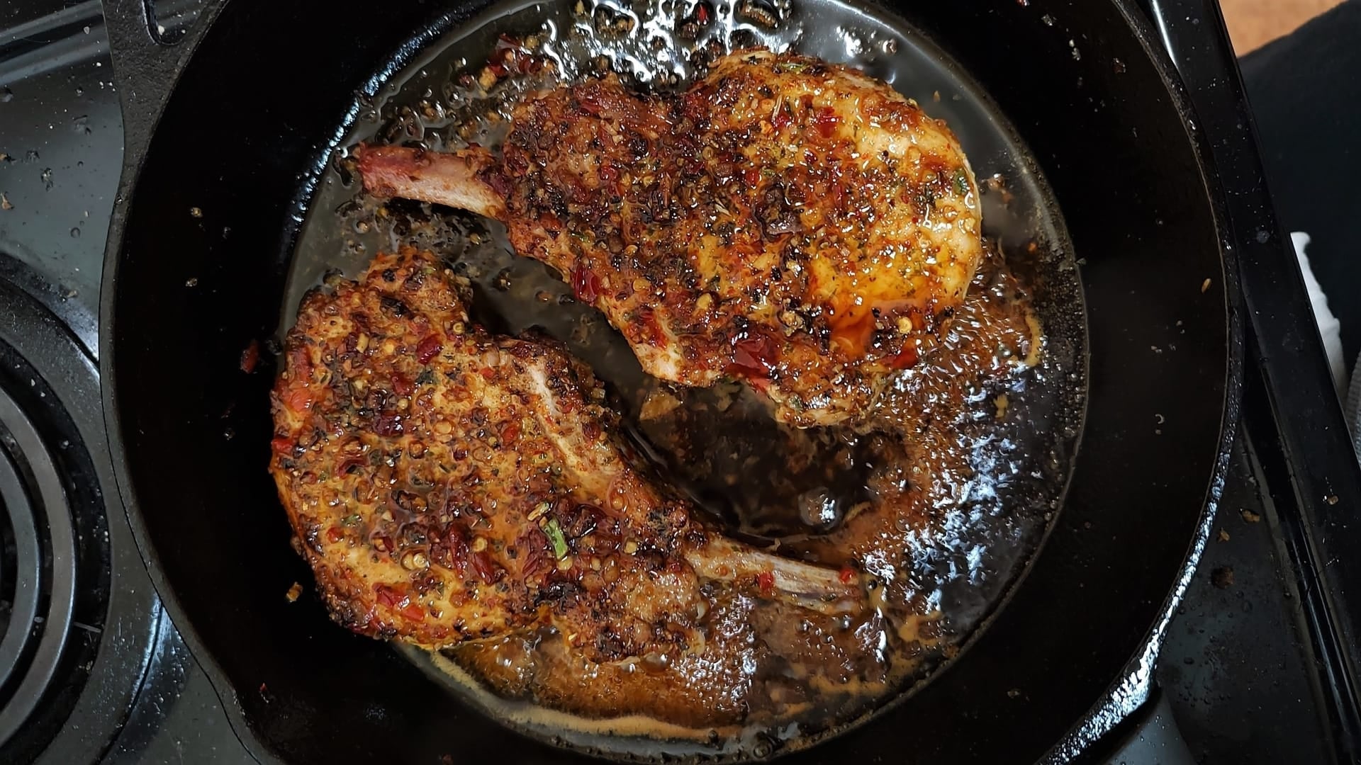 A cast iron pan on a stove top with two bone-in porch chops, smothered in organic farm-fresh Cuban spices from Well Seasoned Table.