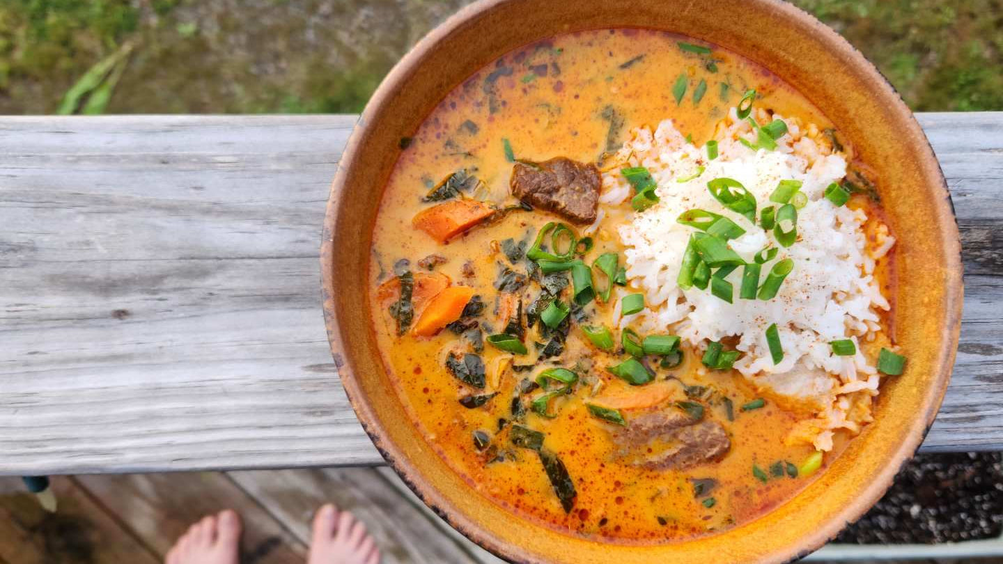 A stoneware bowl of Creamy stew with chunks of beef and rice.