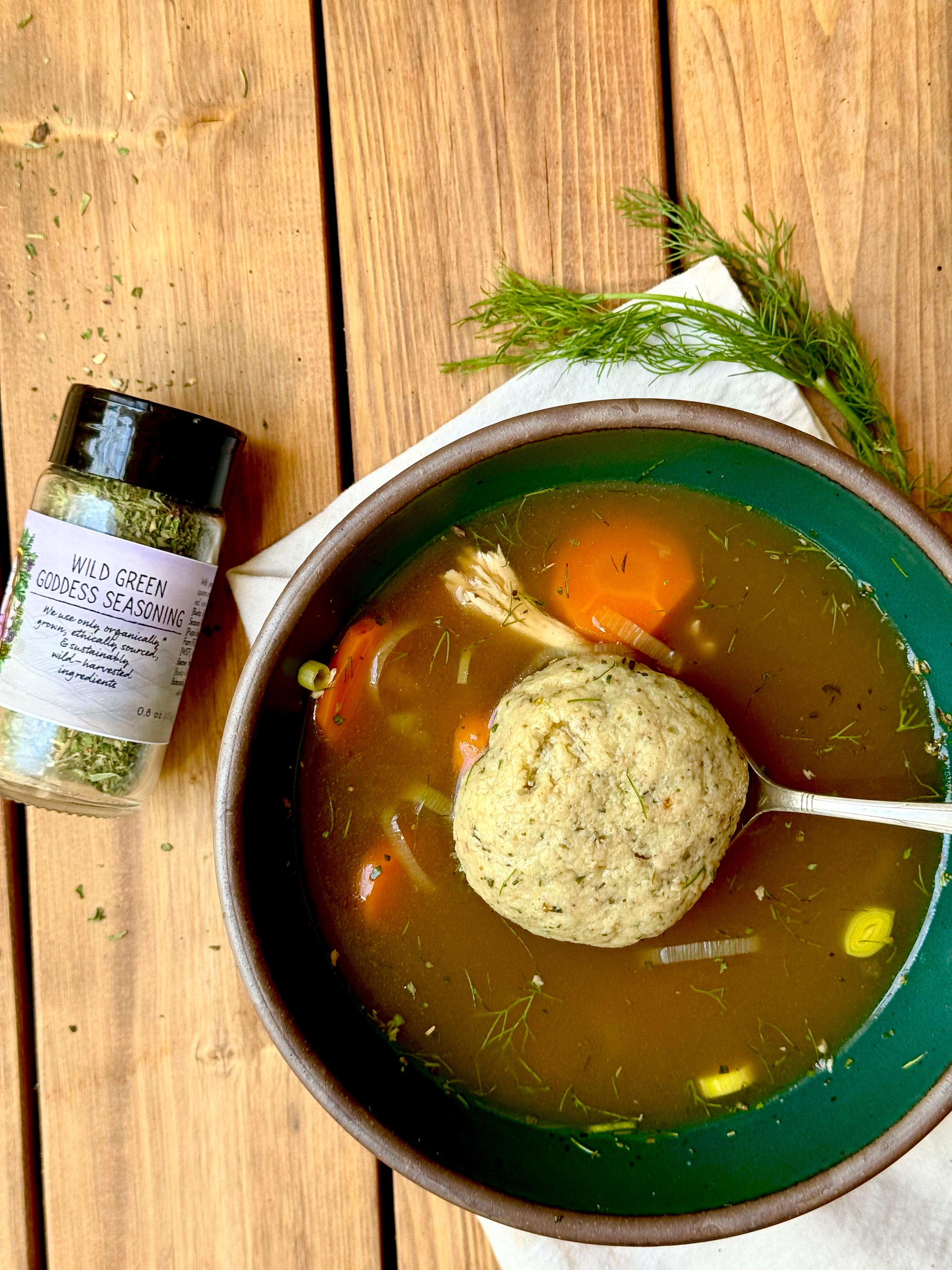 Matzo Ball Soup on Wood Table with herbs and Wild Green Goddess Seasoning by Well Seasoned Table