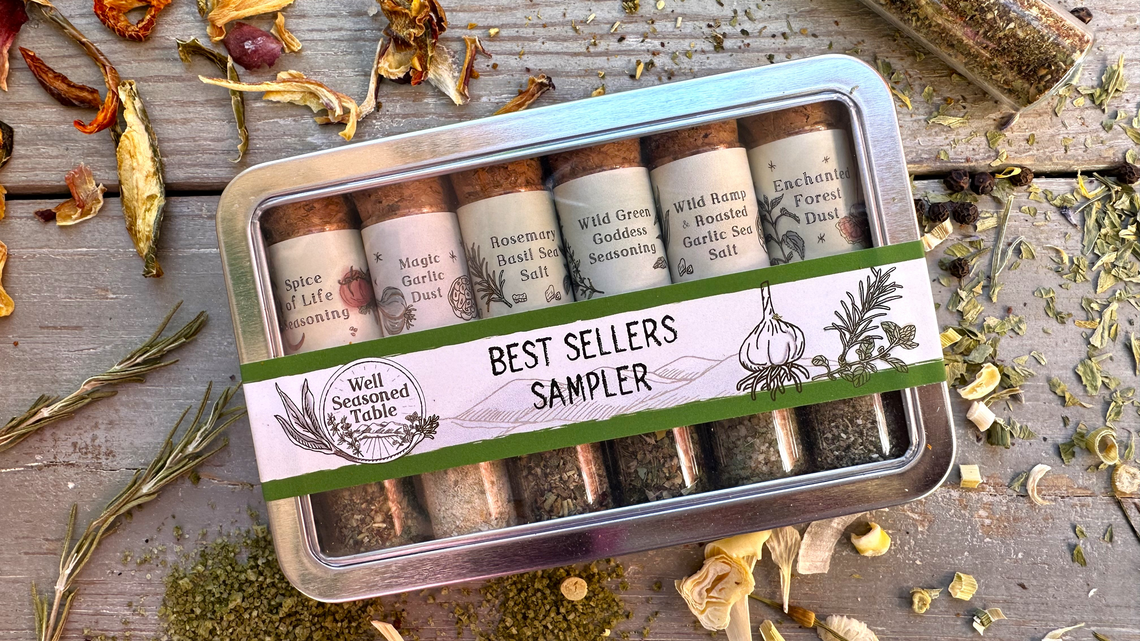 A sampler tin of vials of spices from Well Seasoned Table on a wooden background with organic dried spices around it.