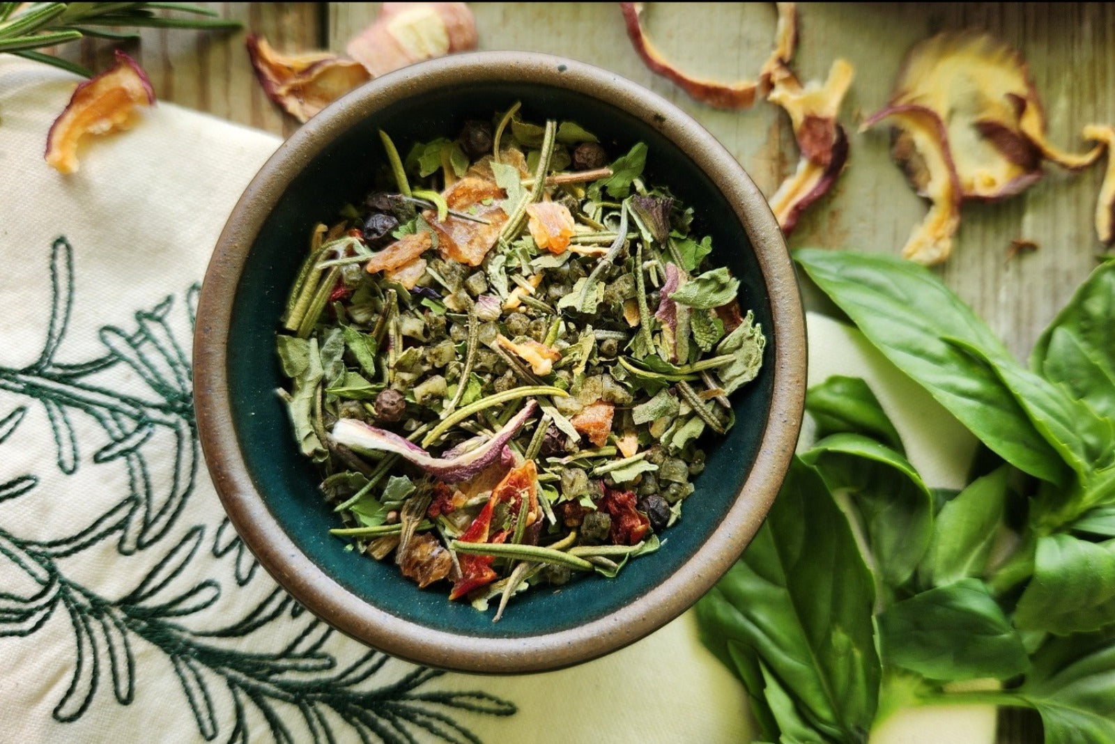 A bowl of Rosemary Basil Sea Salt from Well Seasoned Table with peppers, rosemary, and basil around it.