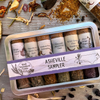 A metal sampler tin with 6 glass vials of organic local spice blends on a wooden background with organic dried spices.