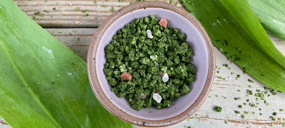 A ceramic bowl of bright green Wild Ramp Sea Salt on a wooden background with fresh ramps around it.