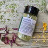 A jar of Emerald Mountain Dust from Well Seasoned Table on a wooden background with a sprinkle of calendula flowers and dried ramps. 