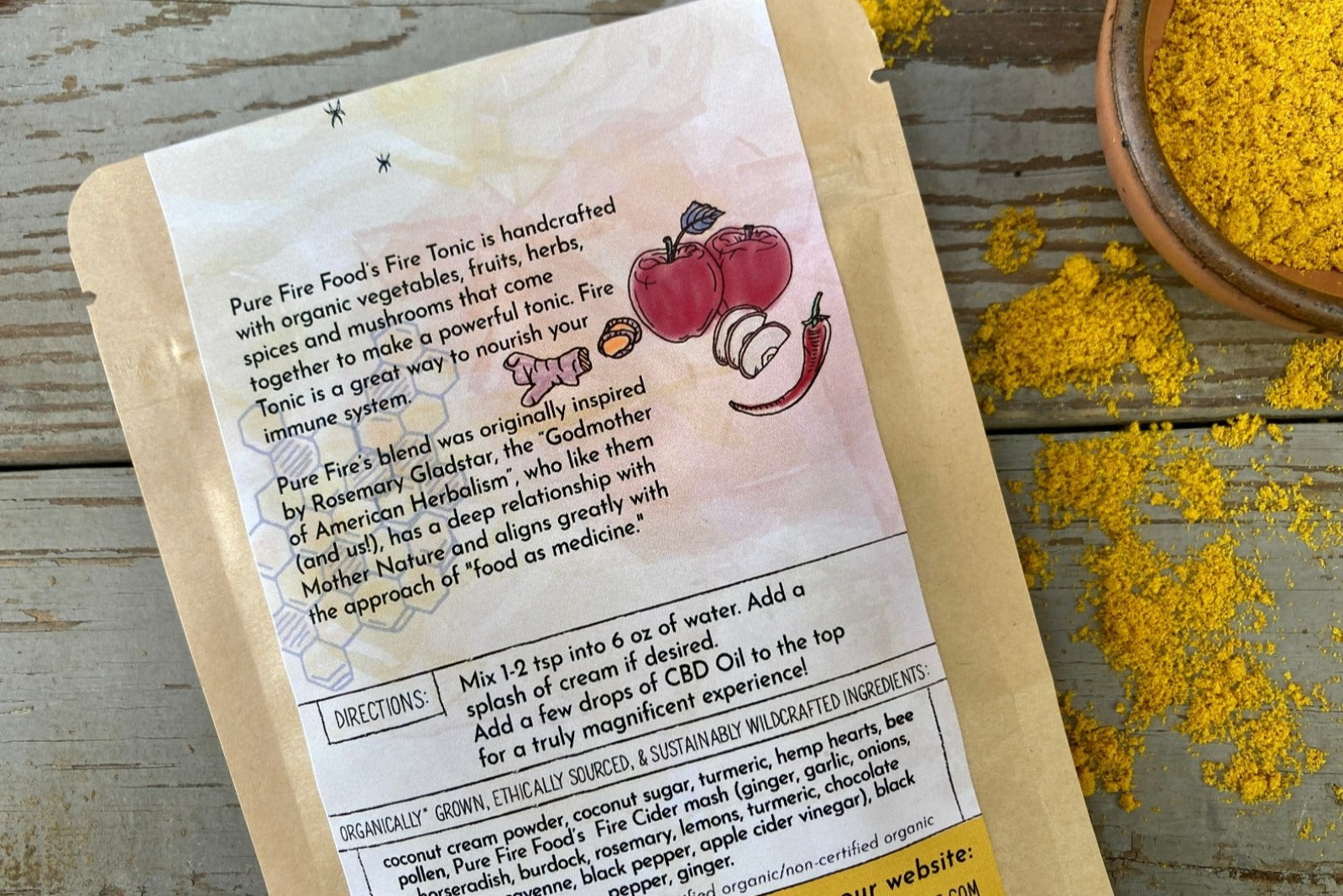 A packet of Fiery Golden Milk from Well Seasoned Table on a wooden background with fall leaves and a bowl of golden milk powder.