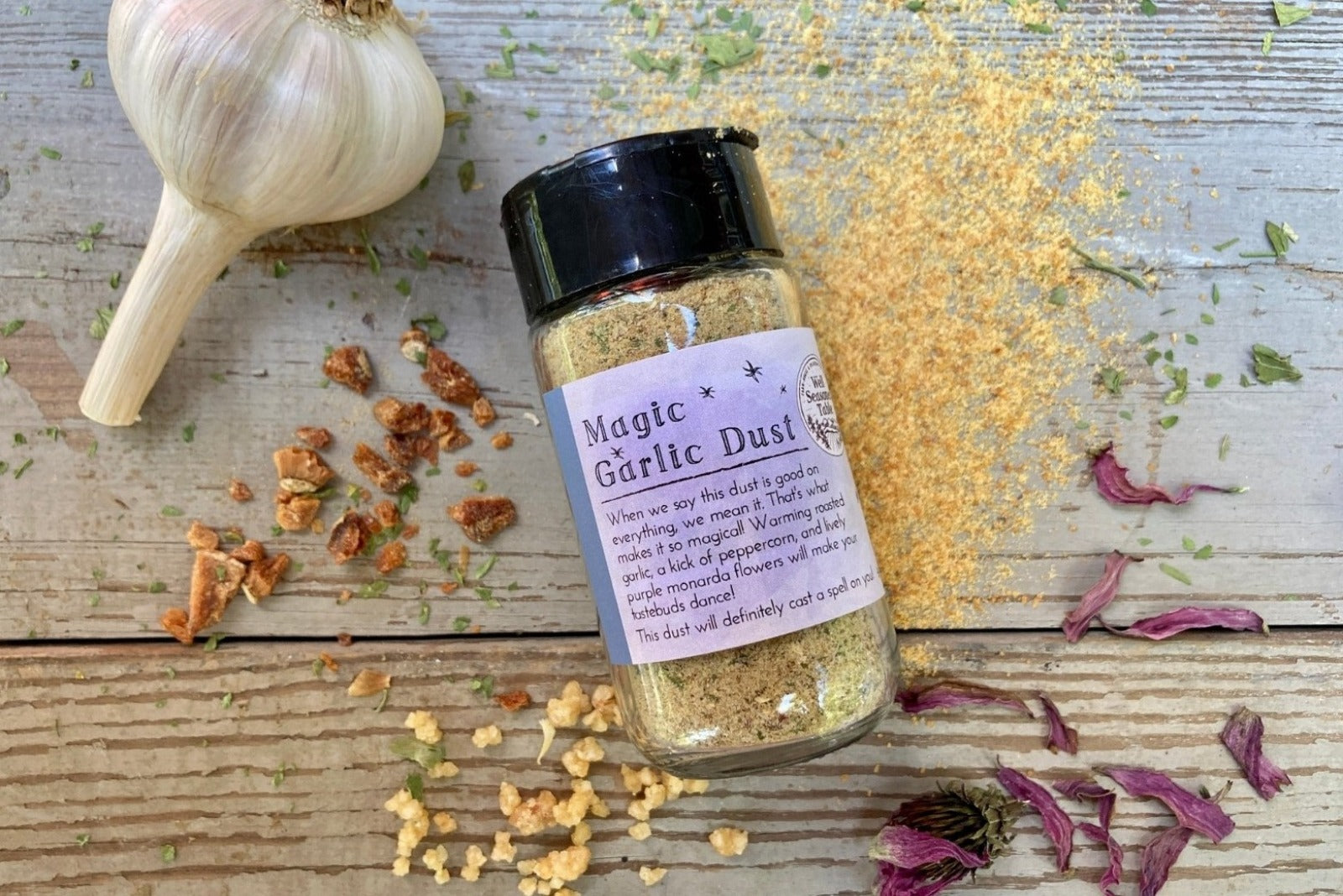 A glass jar of Magic Garlic Dust from Well Seasoned Table, a spice shop, on a wooden background.