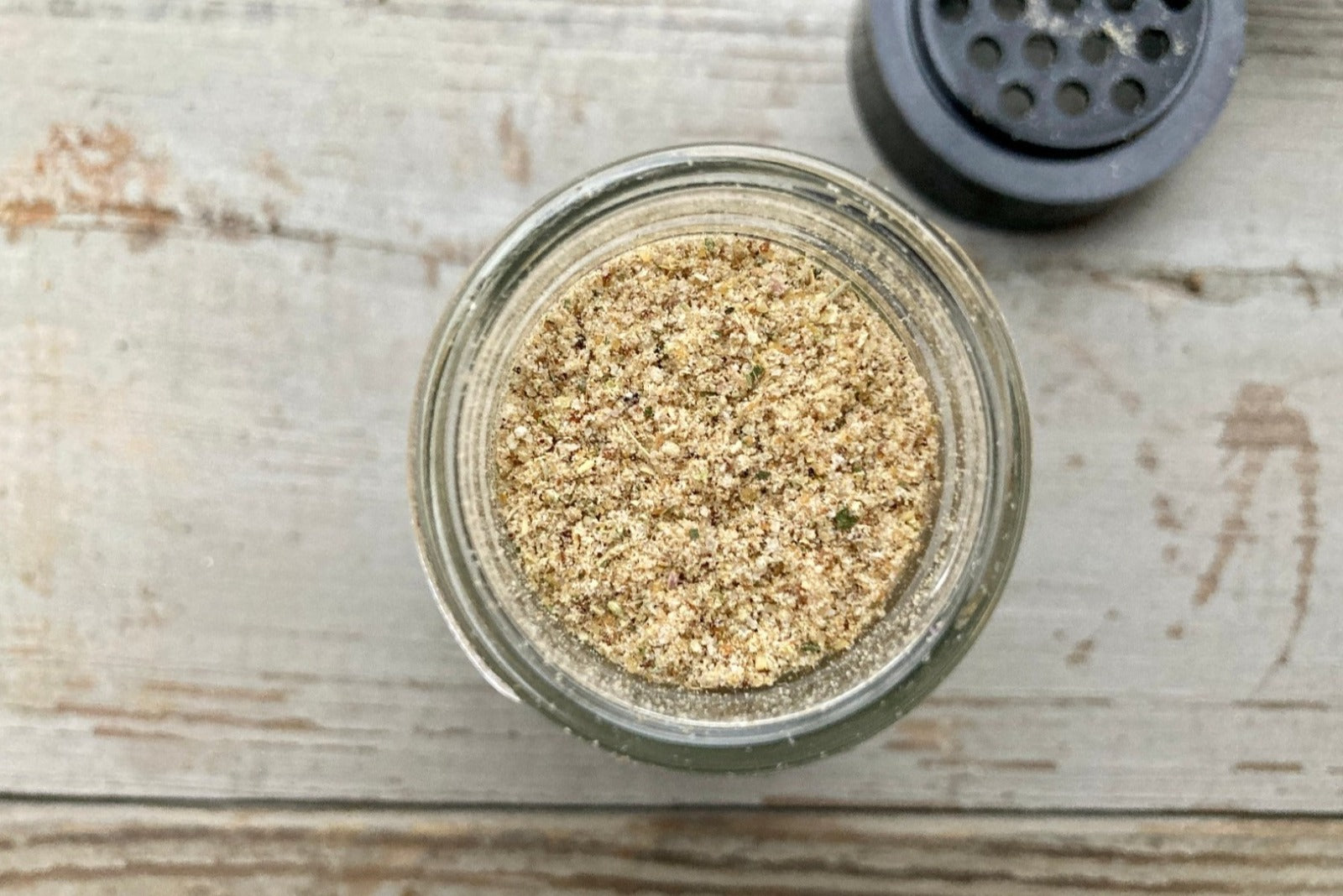 A glass jar of Magic Garlic Dust from Well Seasoned Table, a spice shop, on a wooden background.