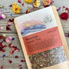 Up close of a packet of Mountain Sunset Tea on a wooden background surrounded by colorful dried flowers.