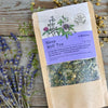  A packet of Sleep Well Tea from Well Seasoned Table on a wooden background with dried lavender and chamomile flowers around it.