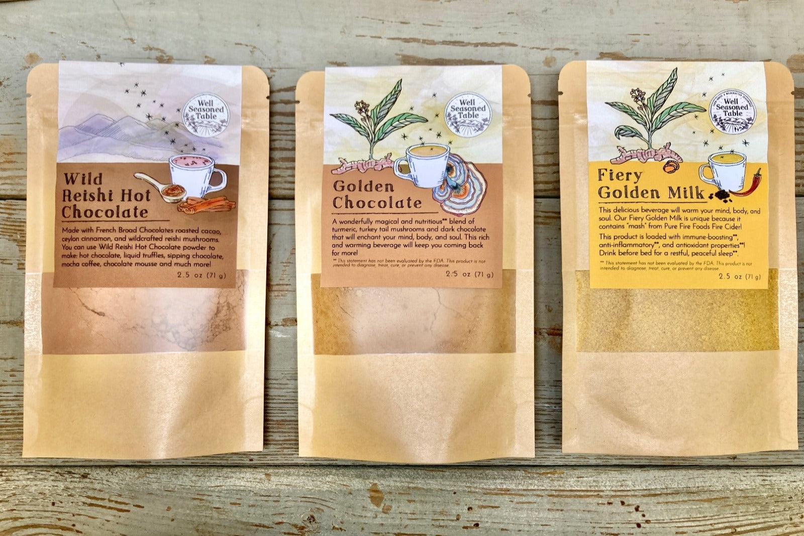 Three packets on a wooden background...Fiery Golden Milk, Wild Reishi Hot Chocolate, and Golden Chocolate from Well Seasoned Table