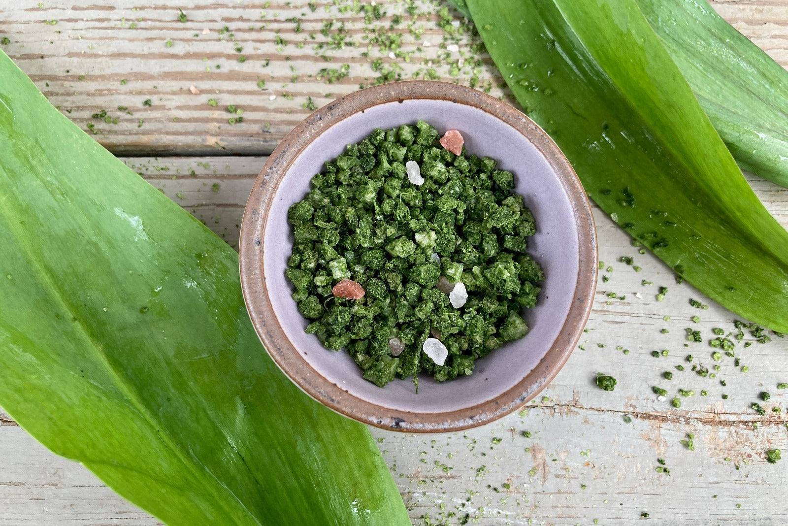 A ceramic mini bowl of Wild Ramp Sea Salt in a grinder jar from Well Seasoned Table on a wooden background with fresh ramps.