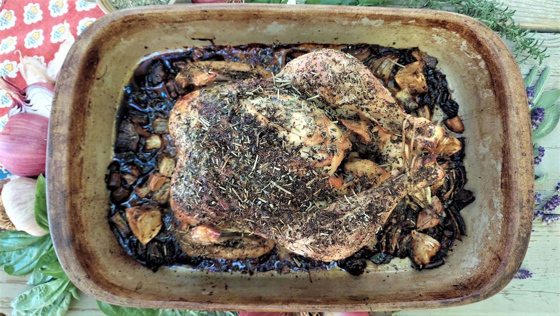 A whole roasted chicken covered with herbs in an earthware roasting pan 