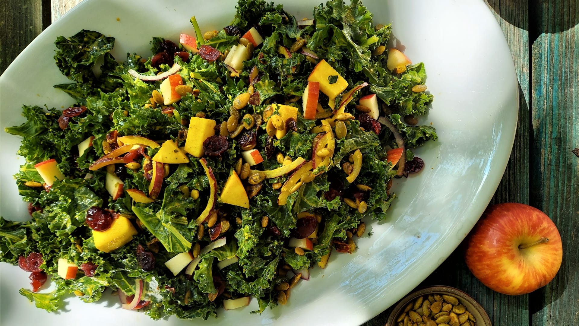 A white platter full of kale salad with apples and cranberries