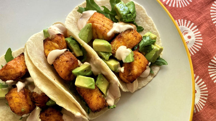 A plate of tacos filled with salmon chunks and avocado on a napkin with sun decor. 