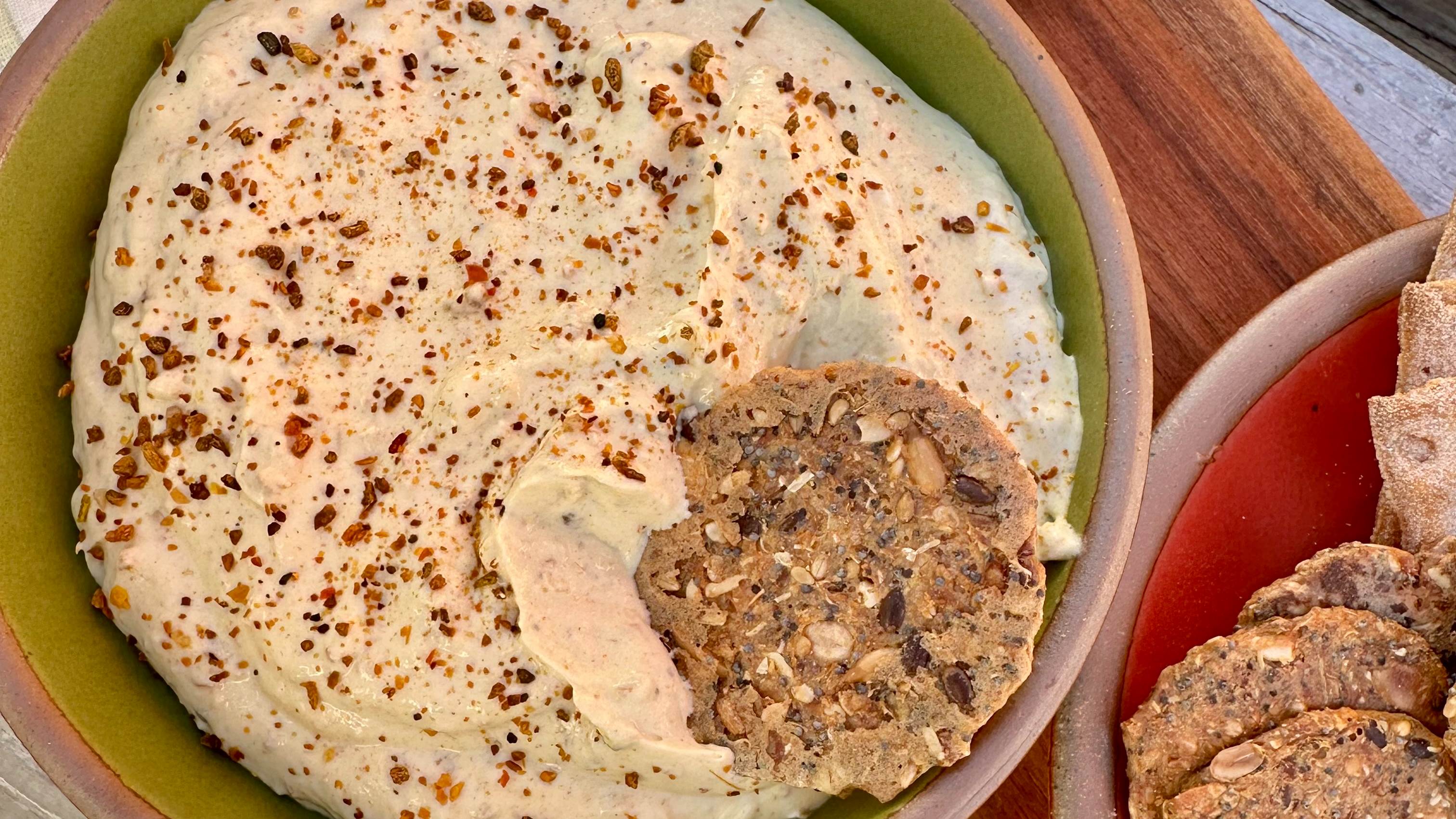 A green bowl of cream dip, covered in Smoked Fire Seasoning from Well Seasoned Table, and a cracker for dipping.