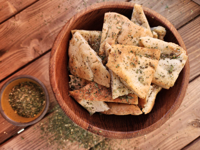 homemade pita chips on wood table with spice of life herbs sprinkled 