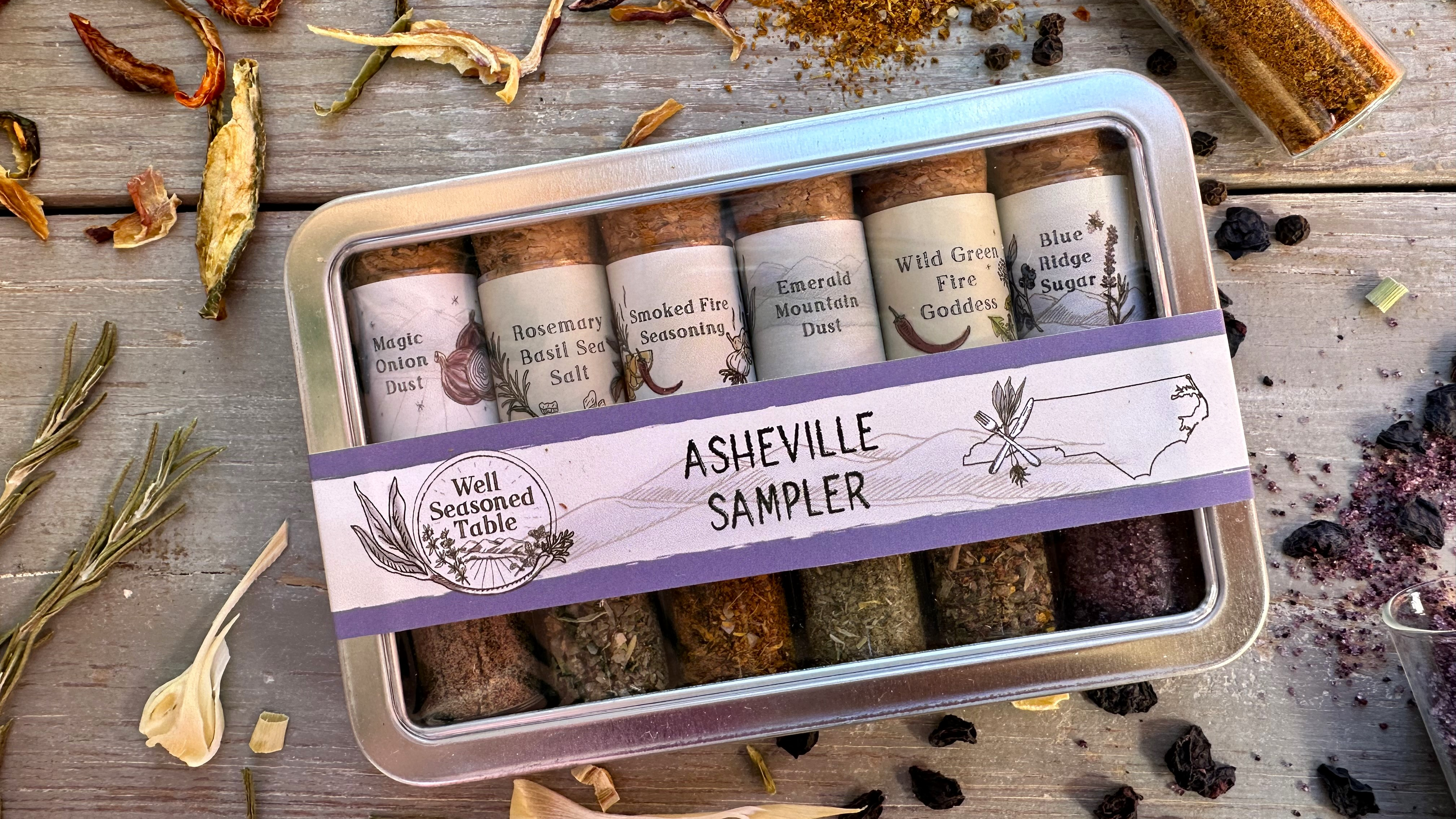 A sampler tin of vials of spices from Well Seasoned Table on a wooden background with organic dried spices and vegetables around it.