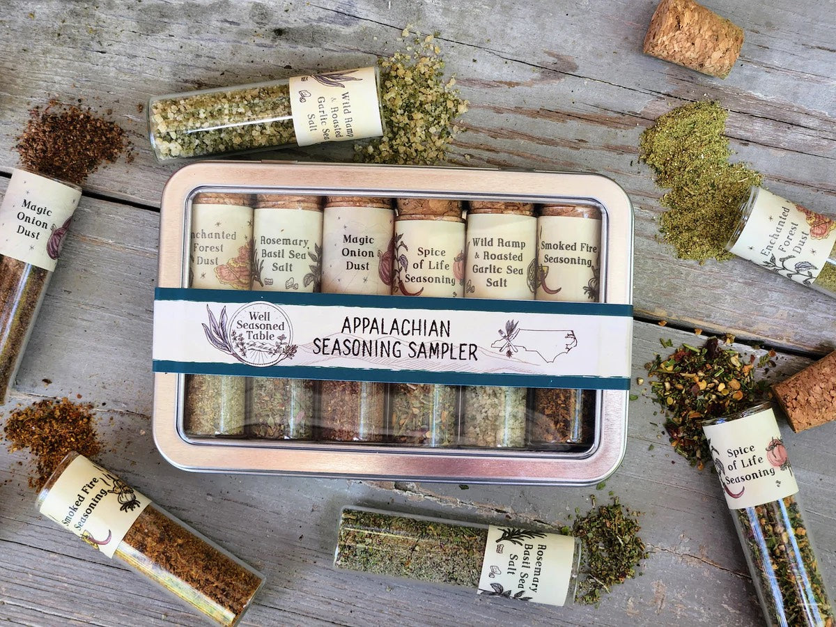 Well Seasoned Table Appalachian Seasoning Sampler Featuring 6 sample vials in a tin box. Display shows the sampler box with sprinkled herbs on a wooden table