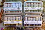  A colorful collection of metal sampler tins with 6 glass vials of organic local spice blends on a wooden background with organic dried spices.