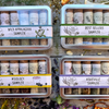 A colorful collection of metal sampler tins with 6 glass vials of organic local spice blends on a wooden background with organic dried spices.