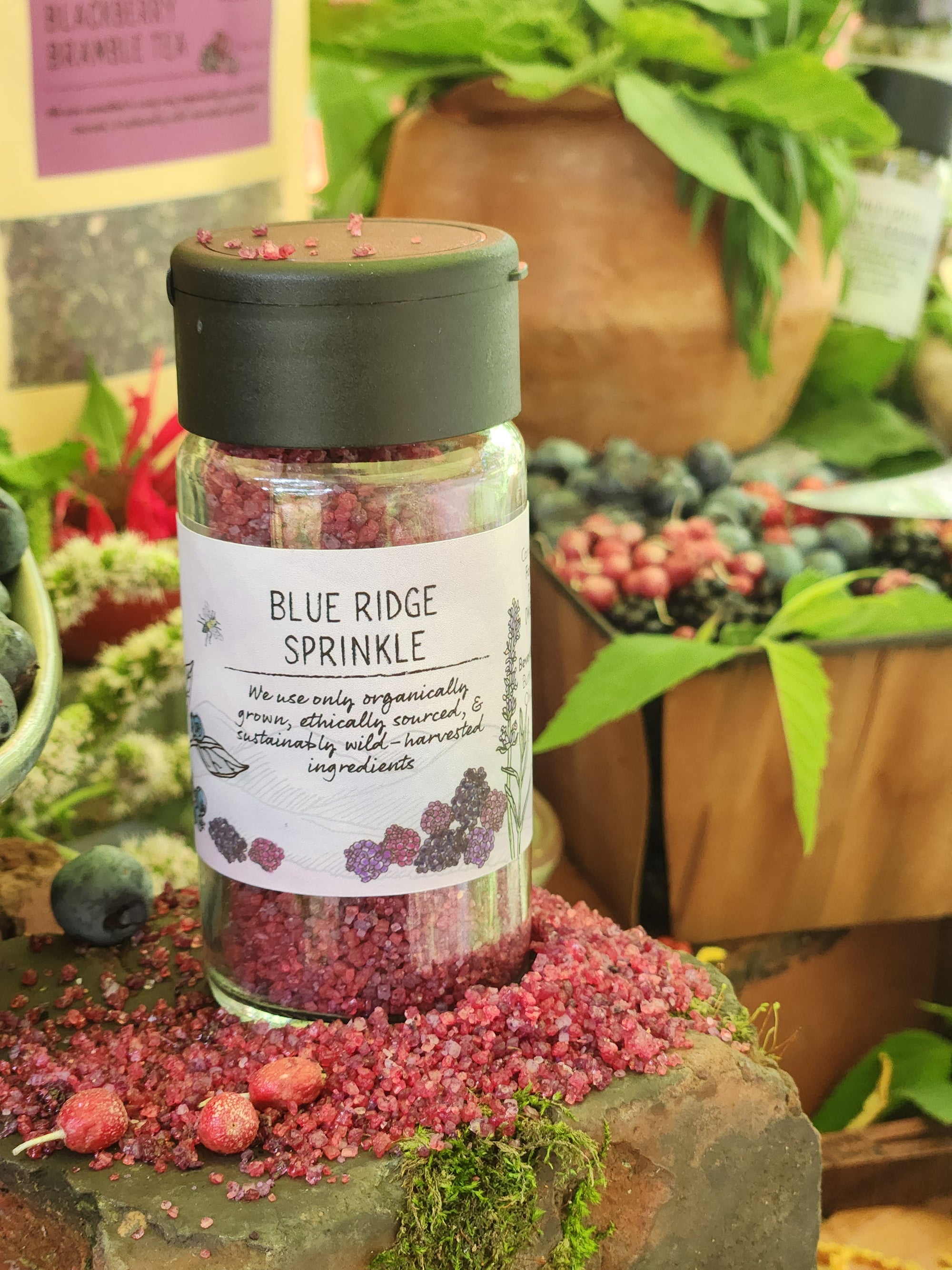 Bottle of Blue Ridge Sprinkle surrounded by an assortment of fresh berries and green herbs