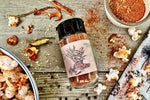 A ceramic bowl of Thai Red Curry Seasoning from Well Seasoned Table on a wooden background with organic dried red peppers, ginger, and black peppercorns.