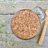 The top of a Glass jar with cork and label and a small wooden spoon on a wooden background with dried herbs, garlic, and sumac around it.