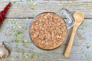 The top of a Glass jar with cork and label and a small wooden spoon on a wooden background with dried herbs, garlic, and sumac around it.