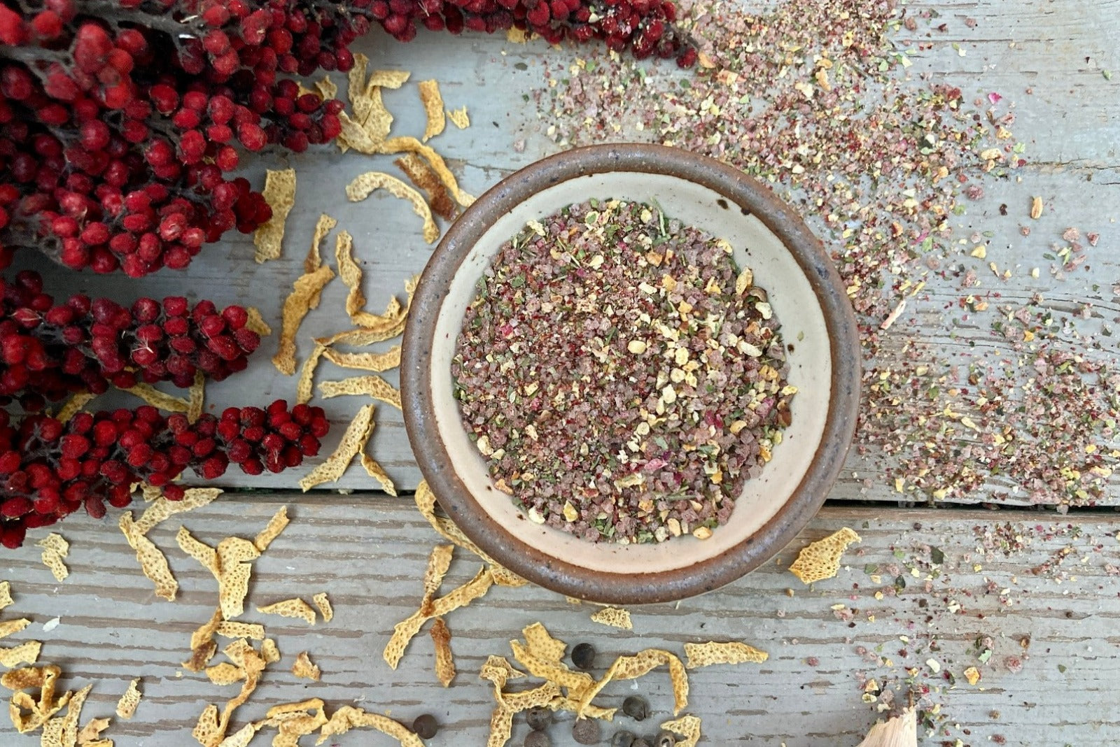 A bowl of Appalachian Lemon Sea Salt, an organic infused sea salt from Well Seasoned Table on a wooden background with dried lemon peel and wildcrafted sumac.