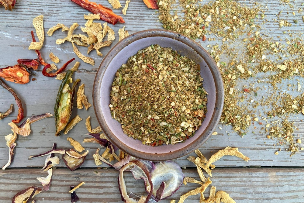 A bowl of Cuban Seasoning from Well Seasoned Table on a wooden background with a bowl of seasoning and dried onions and peppers.
