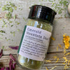A jar of Emerald Mountain Dust from Well Seasoned Table on a wooden background with a sprinkle of calendula flowers and dried ramps. 