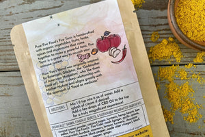 A packet of Fiery Golden Milk from Well Seasoned Table on a wooden background with fall leaves and a bowl of golden milk powder. 