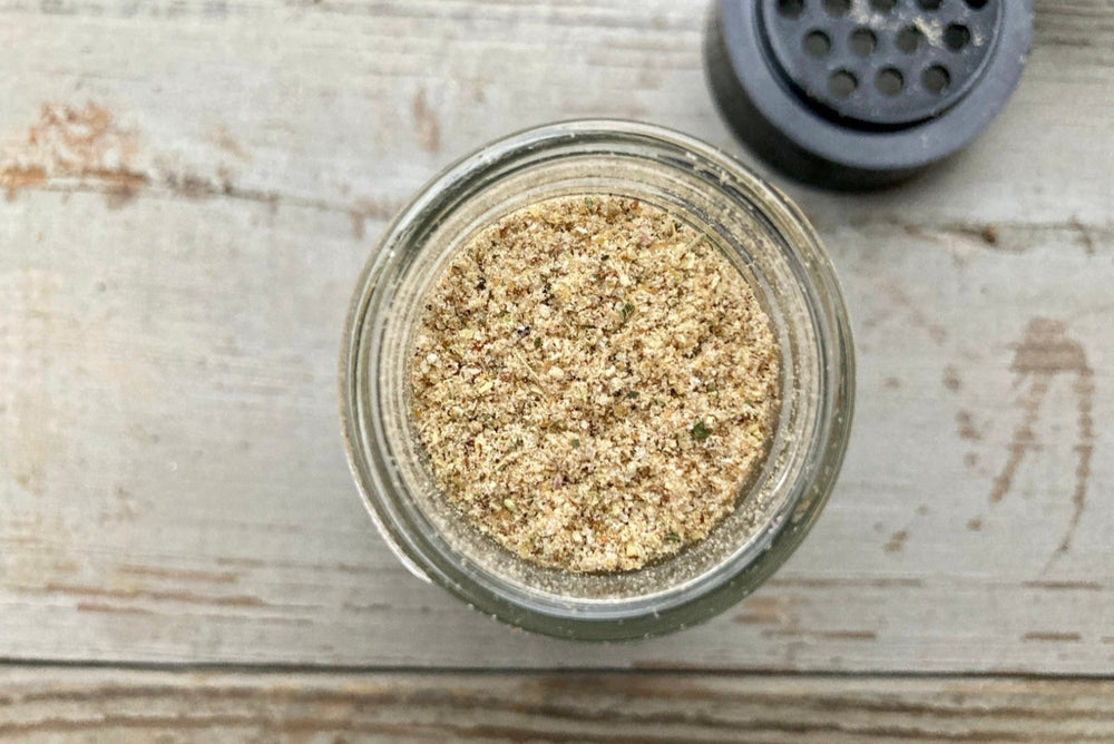 A glass jar of Magic Garlic Dust from Well Seasoned Table, a spice shop, on a wooden background. 