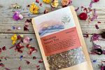The back of a packet of Mountain Sunset Tea on a wooden background surrounded by colorful dried flowers.