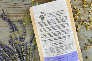 The back of a packet of Sleep Well Tea from Well Seasoned Table on a wooden background with dried lavender and chamomile flowers around it.