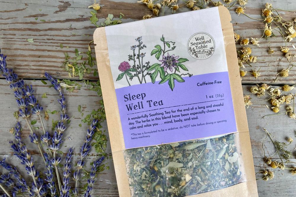 Up close of a packet of Sleep Well Tea from Well Seasoned Table on a wooden background with dried lavender and chamomile flowers around it.