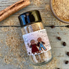 A glass shaker jar of Spiced Gingerbread Sugar Dust from Well Seasoned Table on a wooden background with a bowl of gingerbread sugar and a cinnamon stick.
